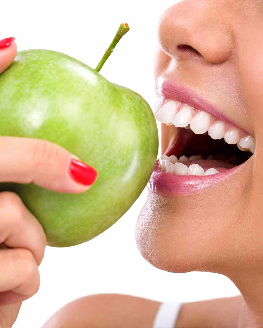A woman biting into a crisp green apple, the restored bite that comes back after All-on-6 at 5D Smiles, Downey CA