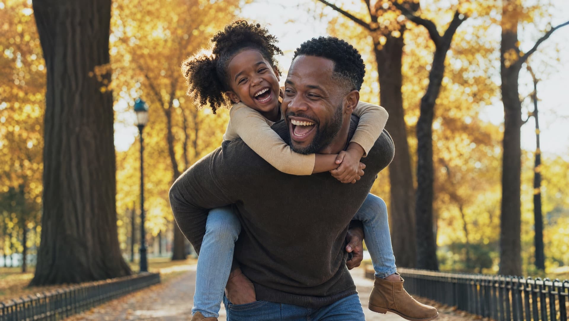 A father giving his young daughter a piggyback ride in a sunlit park, both laughing